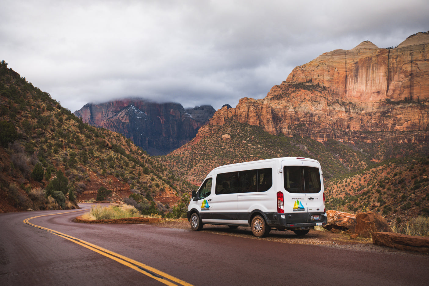 White Wandervans rv rental on a scenic road in Zion National Park, with towering red rock mountains under cloudy skies.