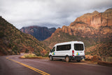 White Wandervans rv rental on a scenic road in Zion National Park, with towering red rock mountains under cloudy skies.