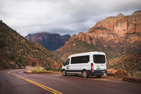 White Wandervans rv rental on a scenic road in Zion National Park, with towering red rock mountains under cloudy skies.