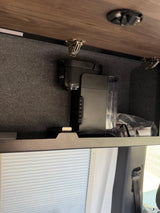 RV rental interior: A Keurig coffee maker and supplies stored in a cabinet with a wire access port, above window blinds.