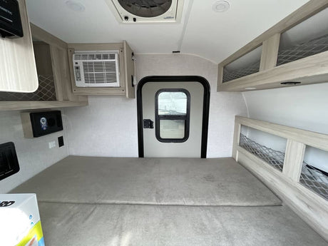 Compact rv rental interior featuring a comfy sleeping area, AC, door, and mesh storage. Ideal for adventurers.