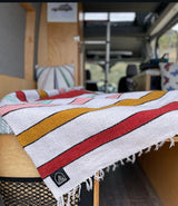 Relax in this RV rental! A cozy bed with a vibrant, fringed striped blanket and pillows, ready for travel.