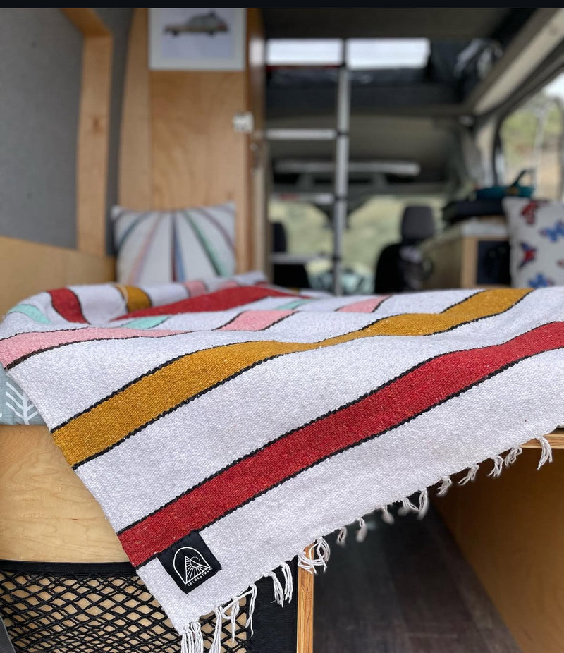 Relax in this RV rental! A cozy bed with a vibrant, fringed striped blanket and pillows, ready for travel. — photo 16