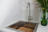 Compact RV rental kitchen features a stainless steel sink, modern faucet, and a cutting board. A vase with greenery is on the counter.