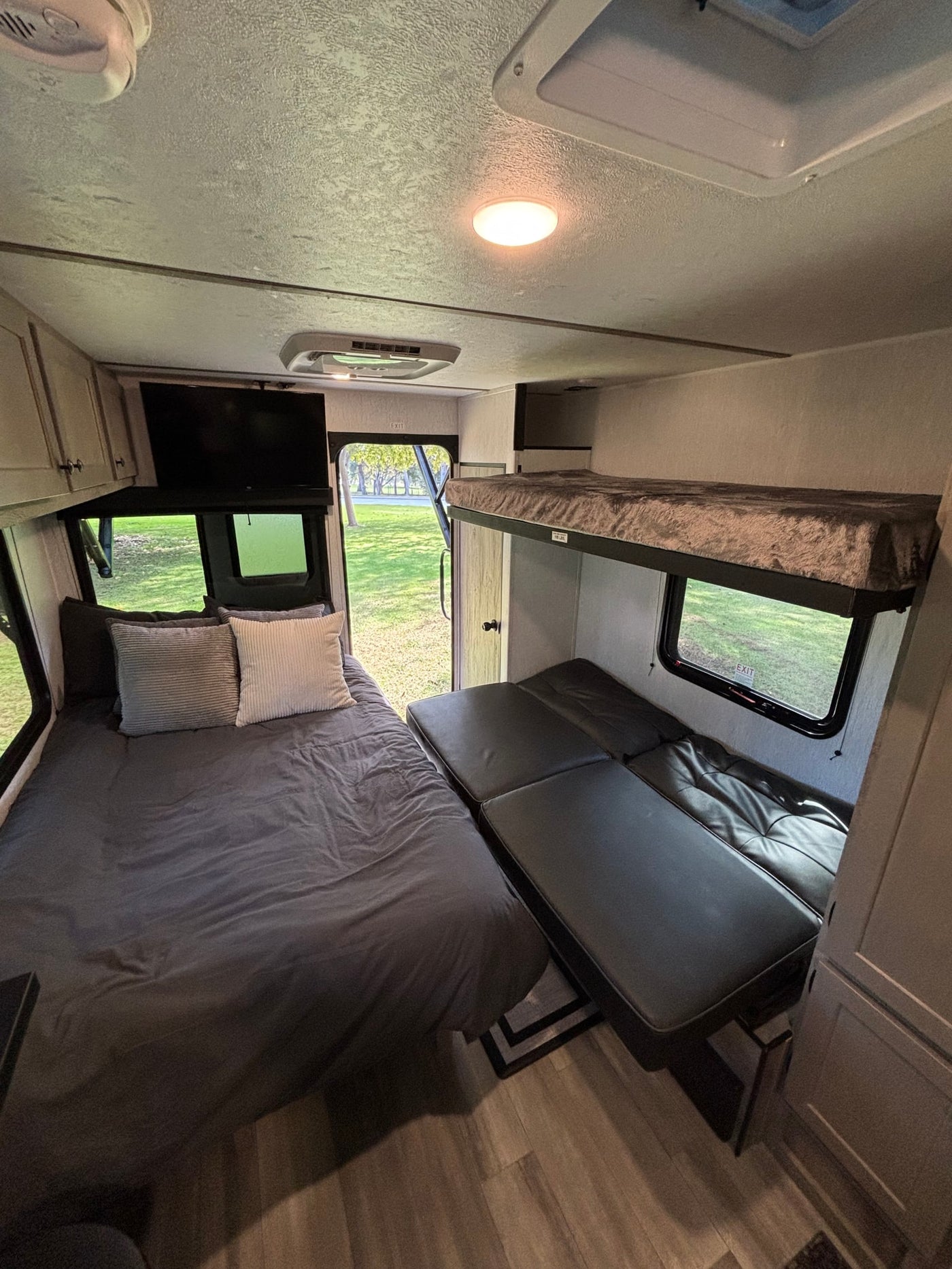 Spacious RV rental interior: main bed, bunk beds, and seating, overlooking greenery outside. — photo 7