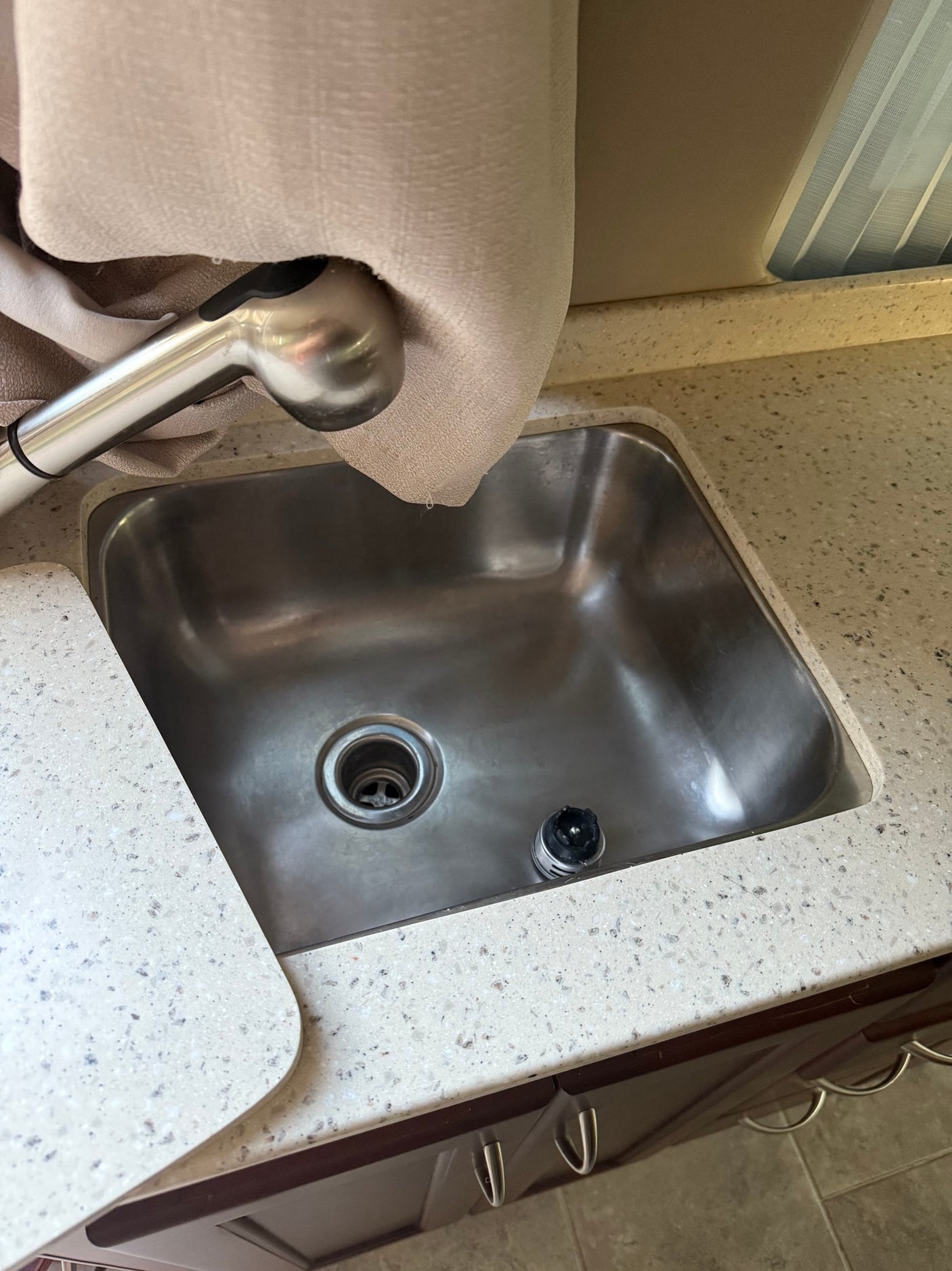 Compact RV rental kitchen sink with pull-down faucet & speckled counter. Curtain shows small drip.