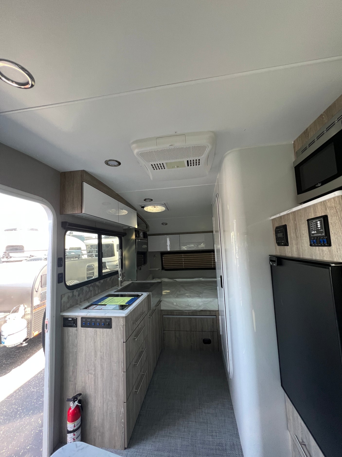 A modern rv rental interior showcasing a compact kitchen, comfortable bed, microwave, and refrigerator, ideal for travel.