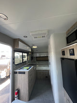 A modern rv rental interior showcasing a compact kitchen, comfortable bed, microwave, and refrigerator, ideal for travel.