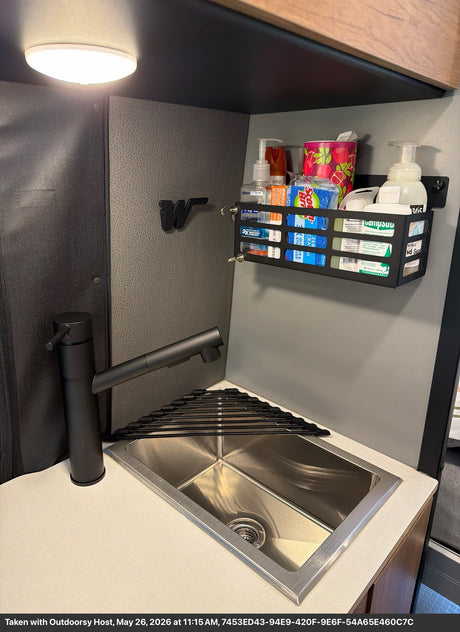 RV rental kitchenette: compact sink with drying rack, black faucet, and wall organizer holding travel essentials.