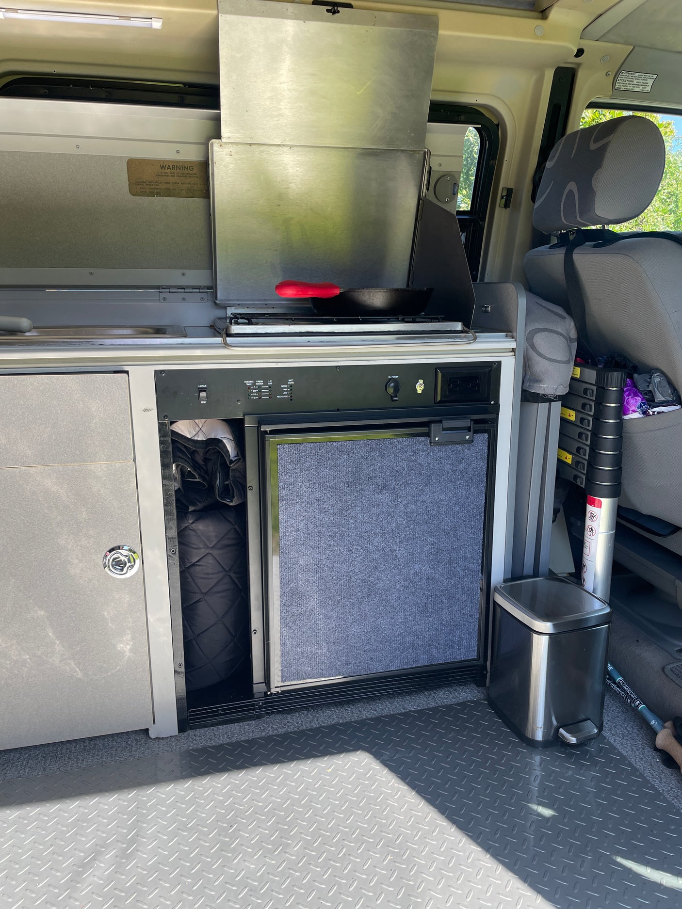 Compact RV rental kitchen setup: stove with pan, fridge, and storage. Ideal for camping and van life adventures.