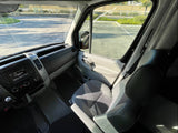 Inside a bright RV rental's front cabin, showing the dashboard, driver & passenger seats, and clear exterior view.