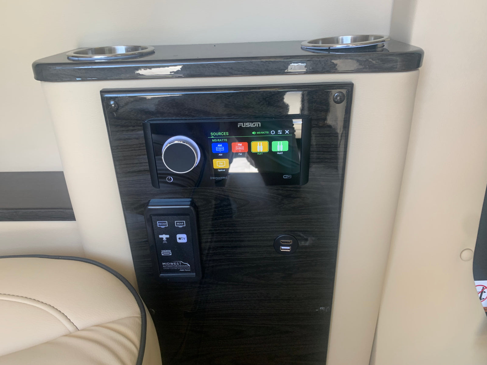 Close-up of a luxury RV rental's custom entertainment panel, featuring a Fusion stereo, Apple TV, HDMI, and USB.