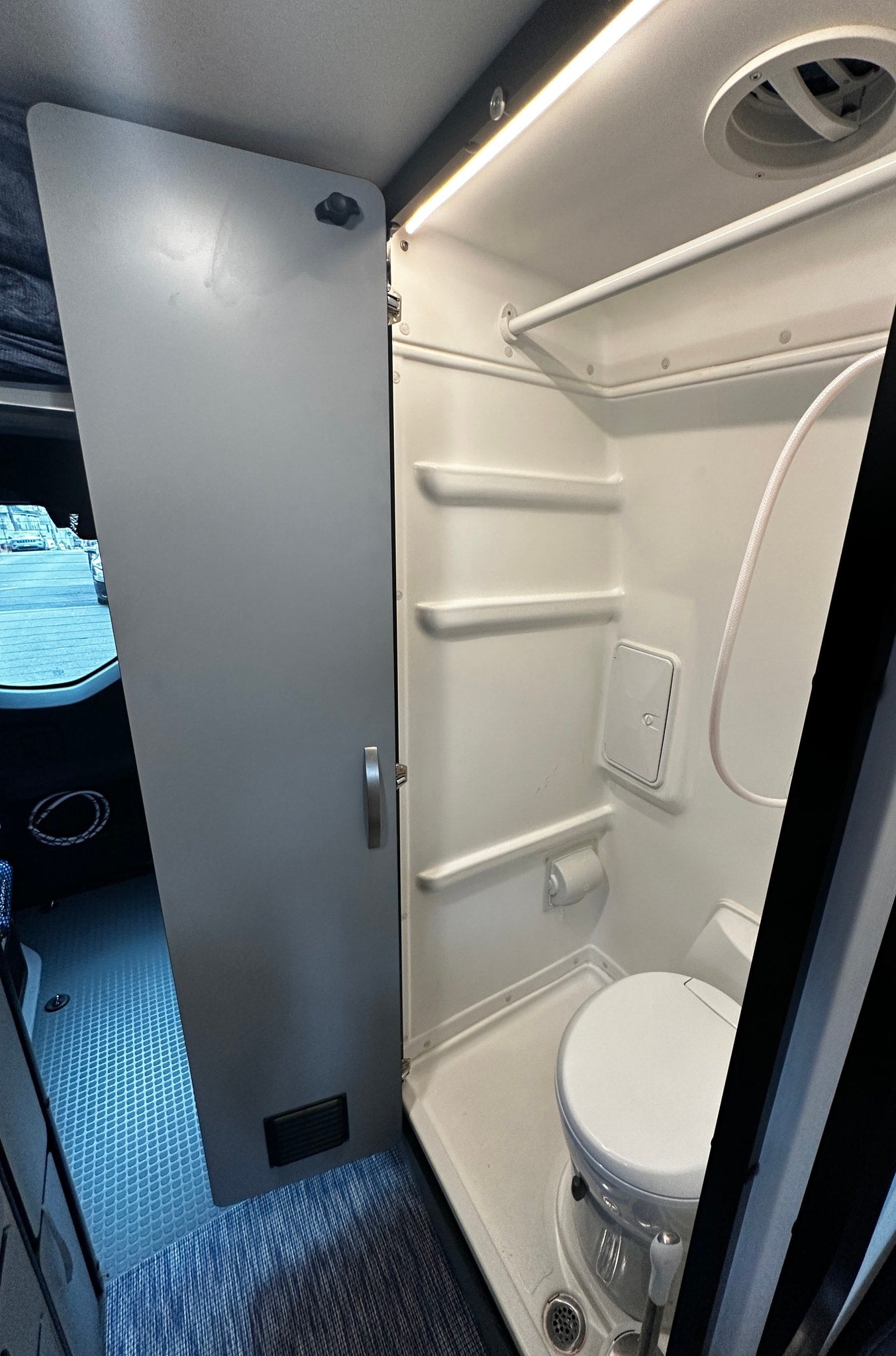 Inside an RV rental: a bright, compact wet bath featuring a toilet, shower, shelves, and ceiling vent. — photo 15