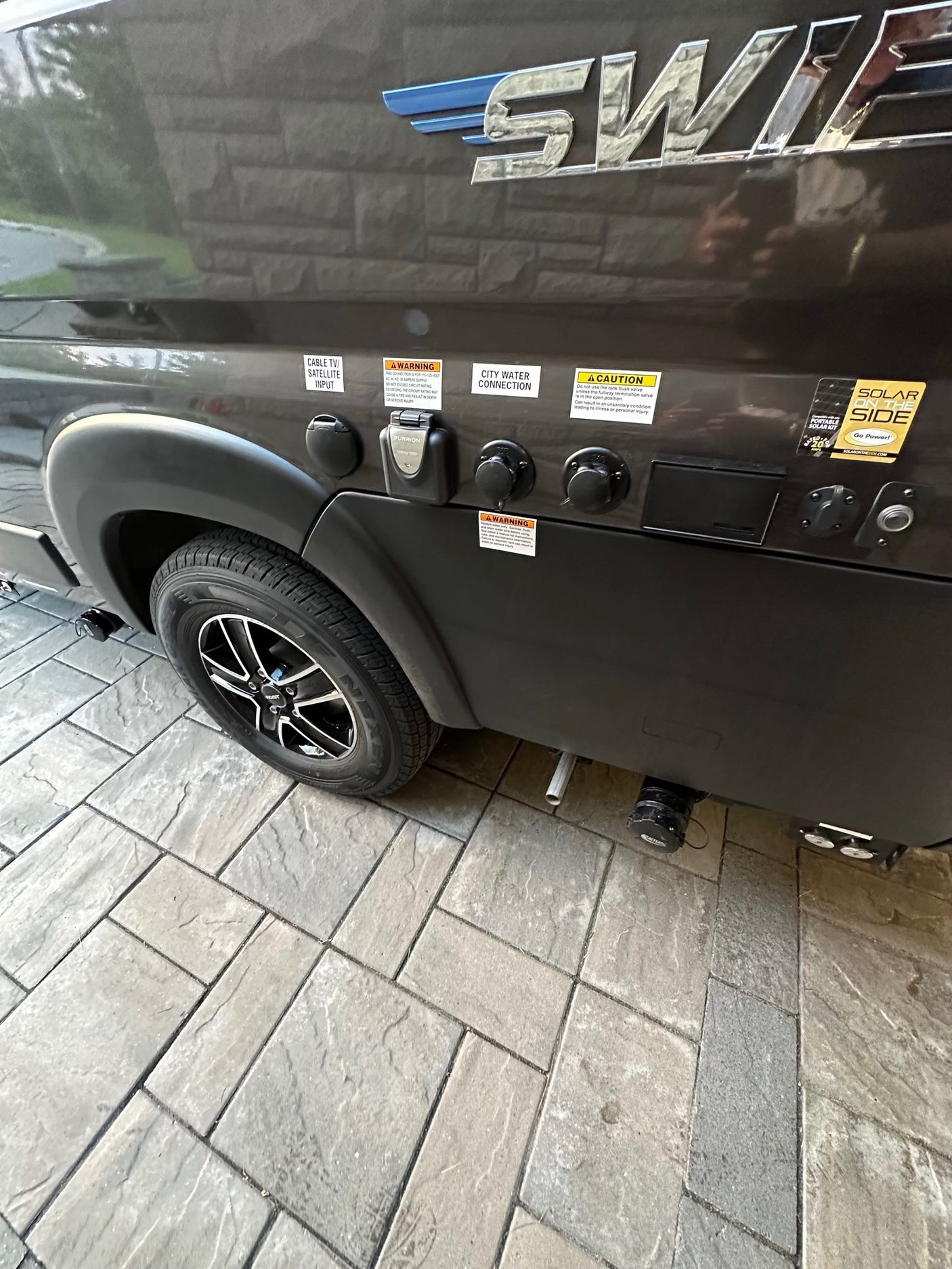 RV rental side with utility connections: cable TV, city water, Furrion electrical, and solar input. Tire visible on paved ground.