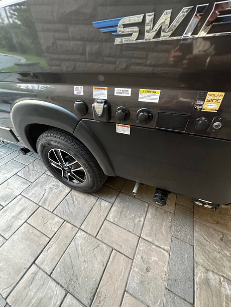RV rental side with utility connections: cable TV, city water, Furrion electrical, and solar input. Tire visible on paved ground.