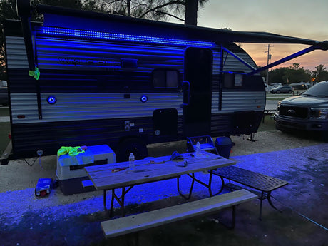 Enjoying the night at an RV rental site! Blue LED lights highlight the camper and picnic area at dusk.