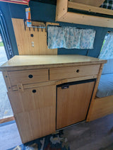 Inside a modern RV rental: bamboo kitchenette with fridge, drawers, and power outlets, optimizing compact camper van living.