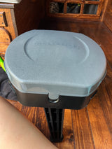 Inside an RV rental, a portable gray Reliance toilet stands on the wooden floor, offering convenient comfort for travel.