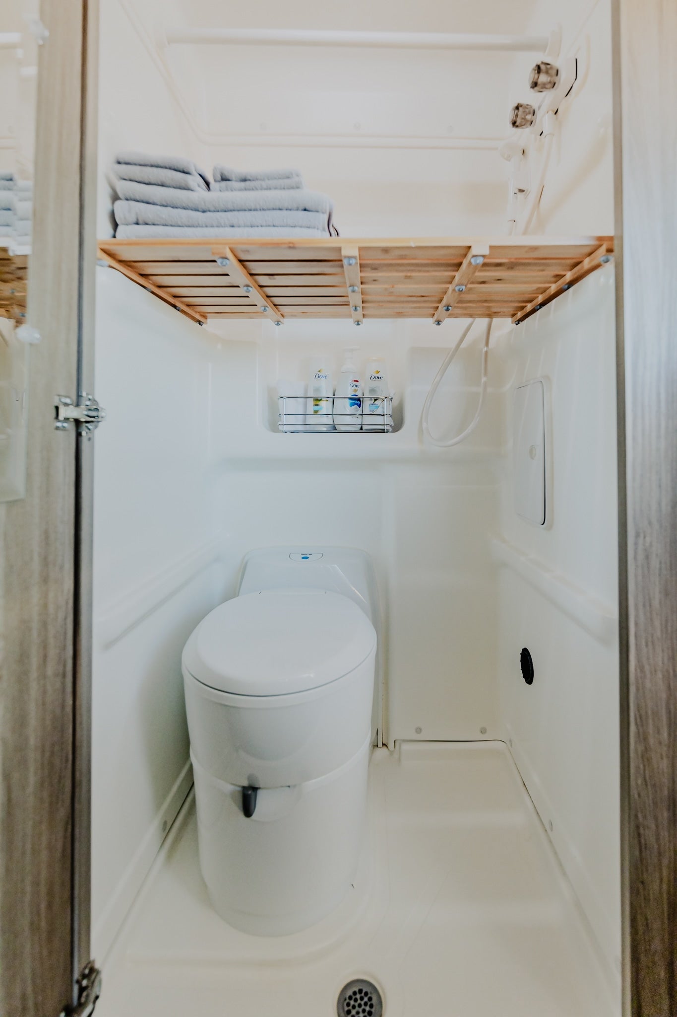 Compact RV rental wet bath, showing a white toilet, shower hose, and a wooden shelf with neatly folded towels. — photo 9