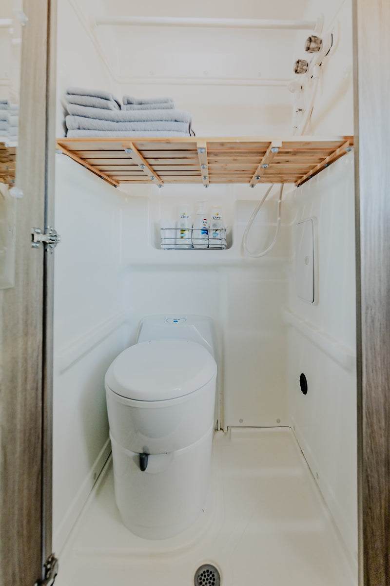 Compact RV rental wet bath, showing a white toilet, shower hose, and a wooden shelf with neatly folded towels. — photo 9