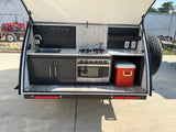 Outdoor kitchen setup in a compact RV rental, complete with sink, stove, microwave, and cooler for effortless camping trips.
