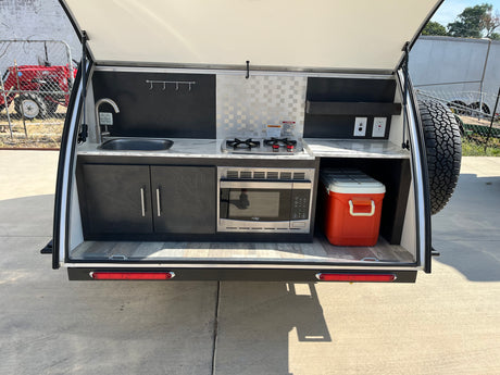 Outdoor kitchen setup in a compact RV rental, complete with sink, stove, microwave, and cooler for effortless camping trips.