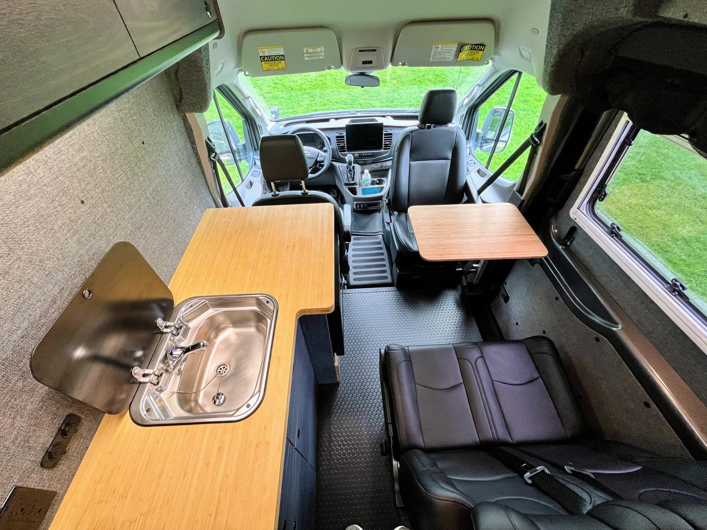 View inside an **RV rental** camper van, showing the front driving area, a flexible rear seating bench, and a kitchenette with a sink.