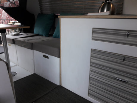Cozy RV rental interior featuring bench seating, a table, and practical cabinetry with striped drawers and a kettle.