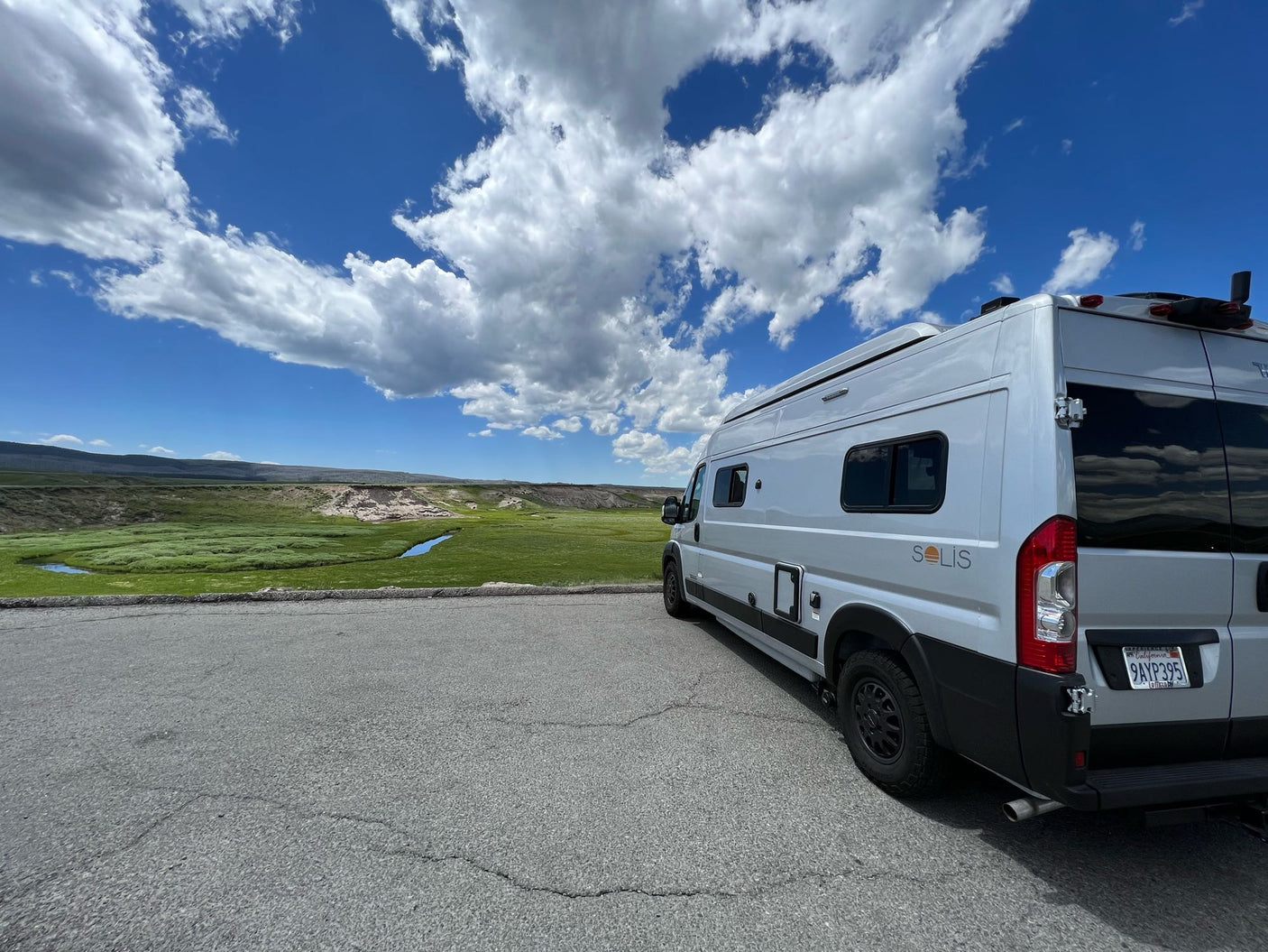 Scenic RV rental: A Winnebago Solis camper van overlooks a lush green valley with a stream under a blue, cloudy sky.