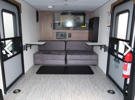 Bright RV rental interior featuring gray sofa seating, TV, and fold-down tables. Dual large doors for easy cargo loading.