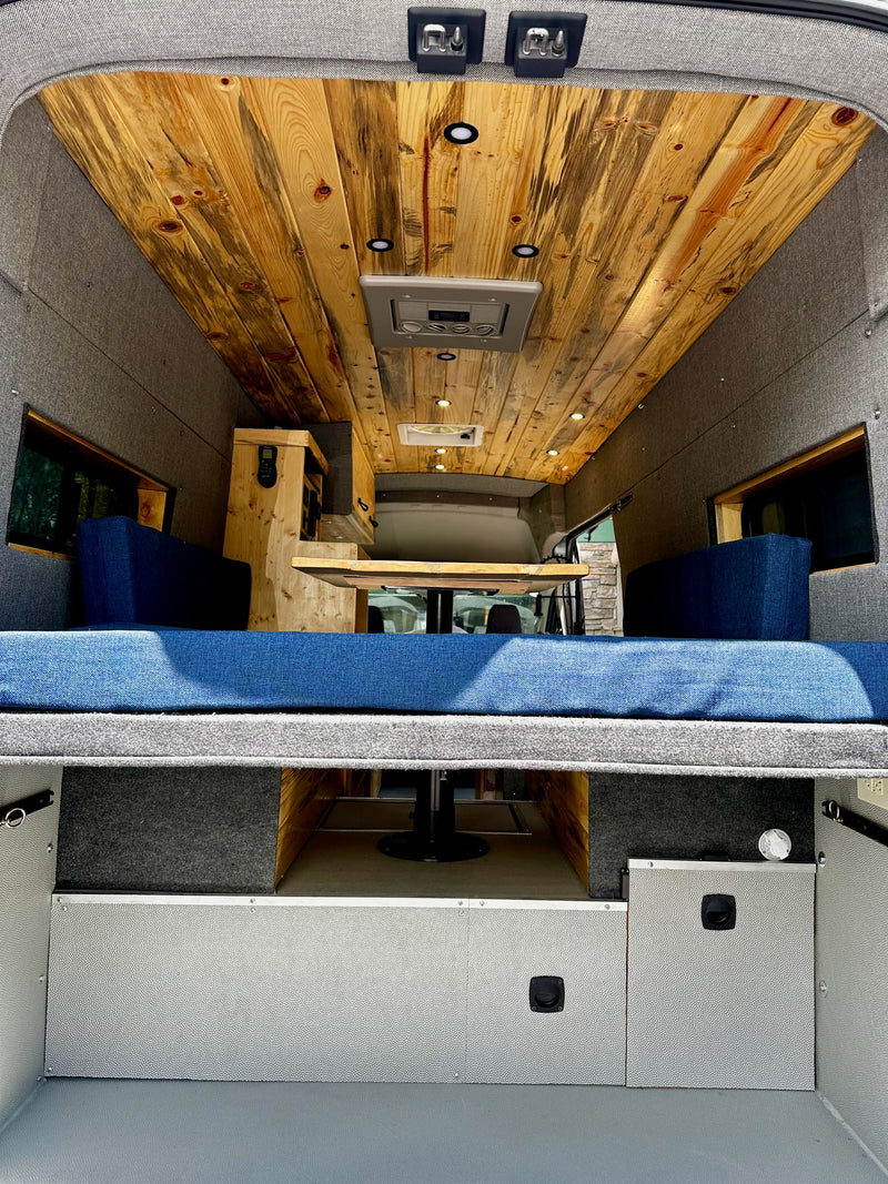 features a roof rack and side ladder. It's parked next to a house.|Top-down view of a gray Ford Transit camper van — photo 4