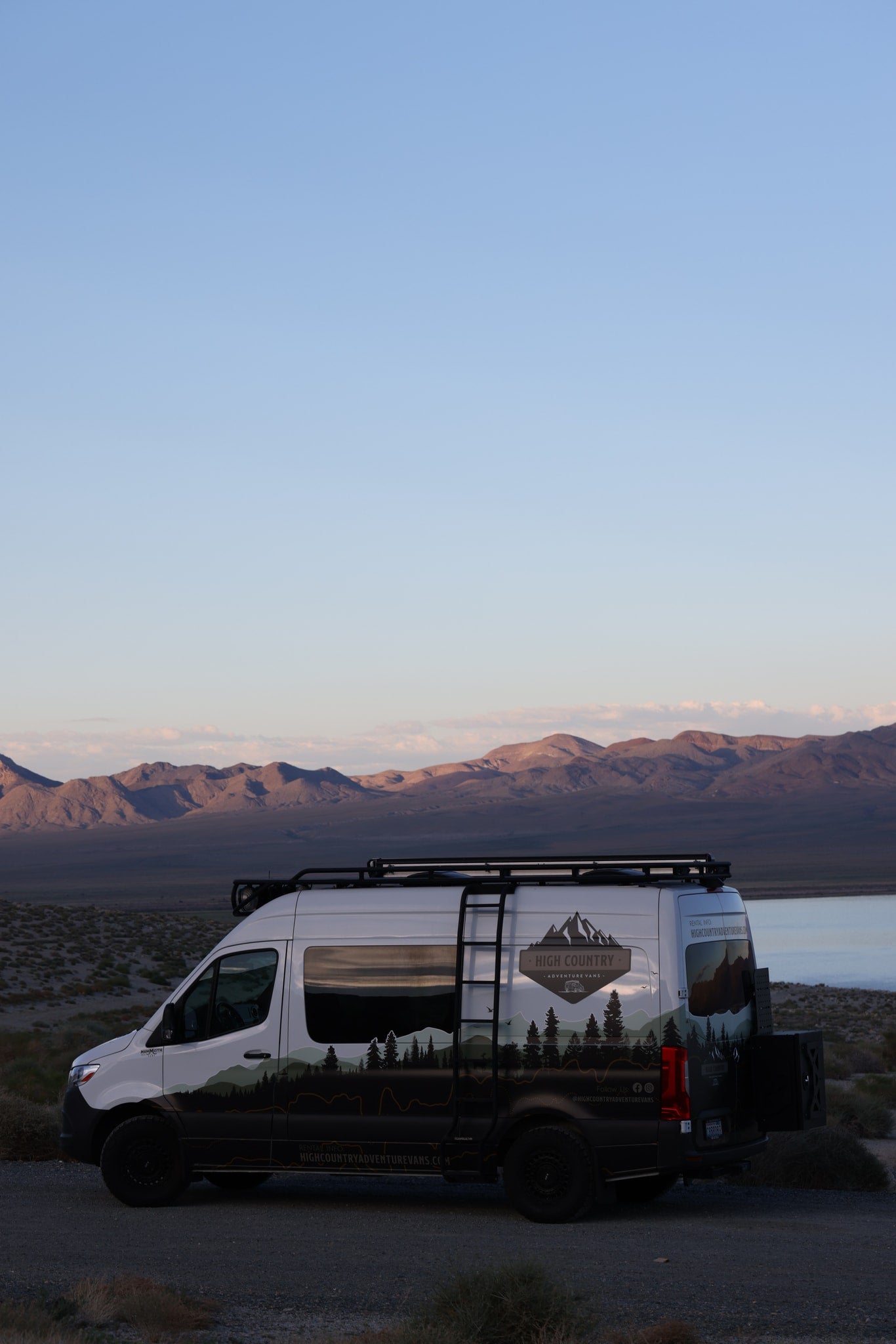 A High Country adventure van RV rental is parked by a lake at dusk, with mountains in the background. Ready for exploring! — photo 15