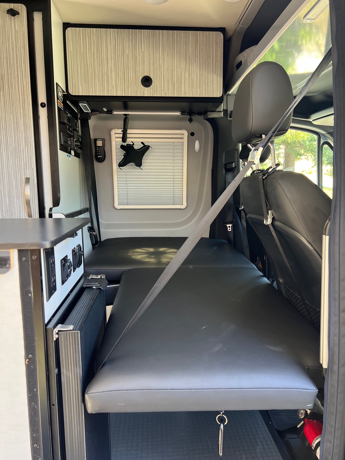 RV rental camper van interior: black padded seating converts to a bed, light wood-grain cabinets, and control panel.