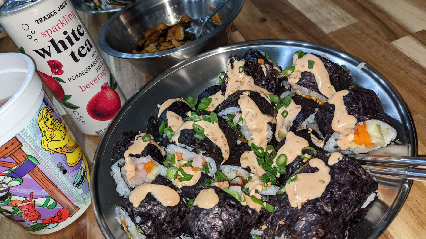 Sauced sushi rolls on a metal plate, a side dish in a bowl, & sparkling tea on a wooden table. Great for an RV rental trip!