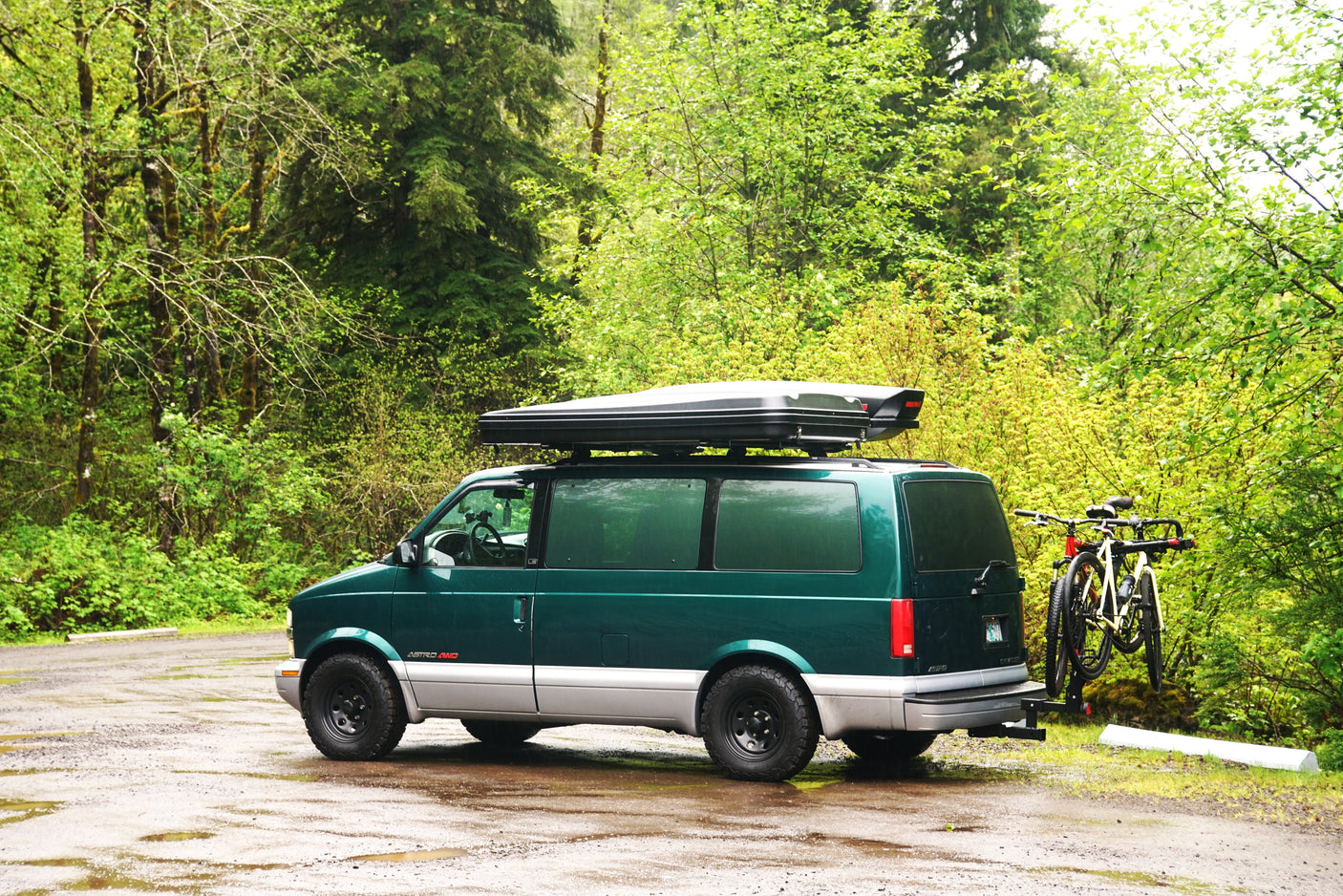This custom dark green adventure van, equipped with a roof cargo box and bike rack, is ideal for an RV rental outdoor trip.