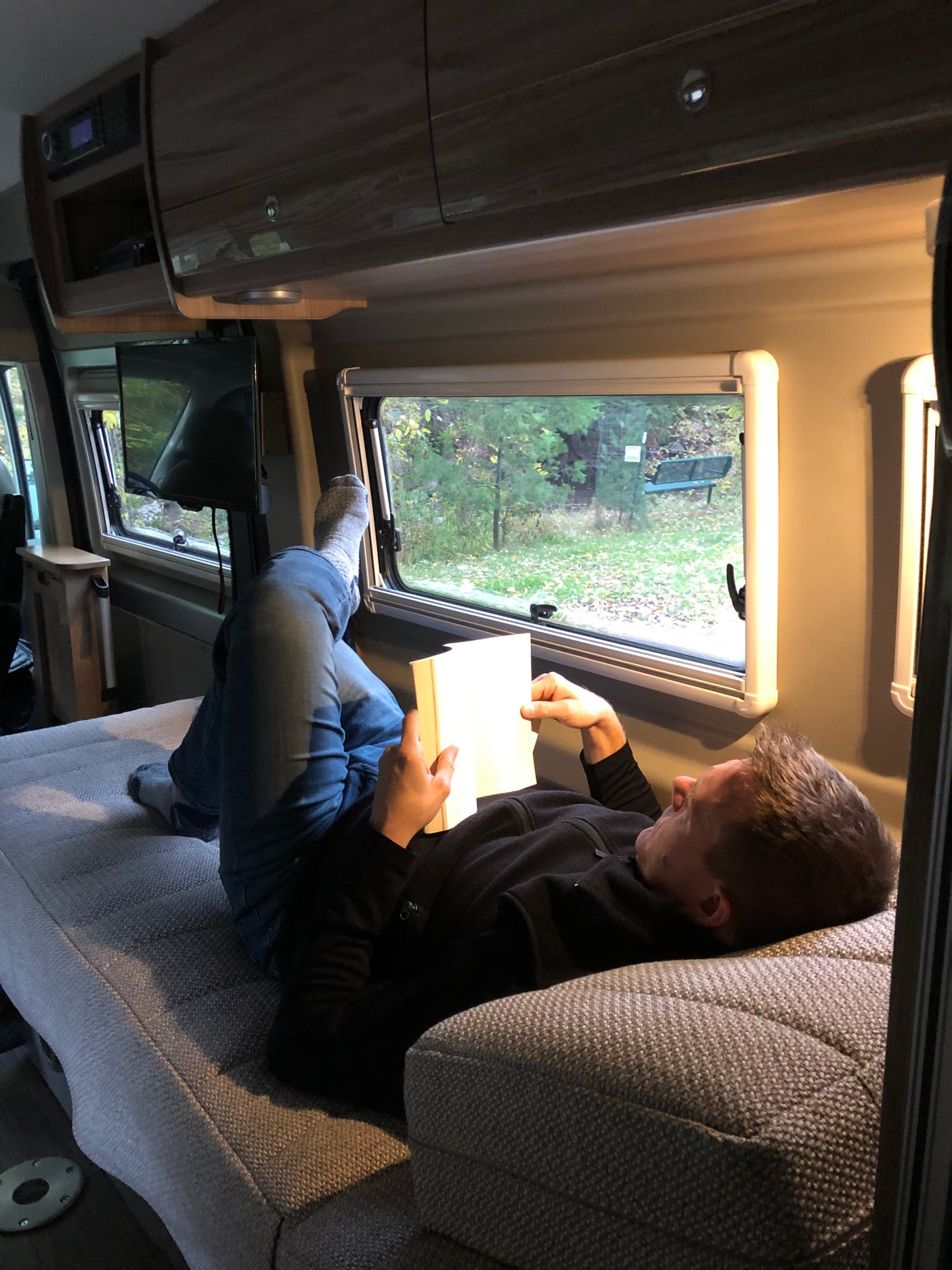 Relaxing in an RV rental: A person reads a book with feet up, enjoying the nature view from inside their cozy camper van.