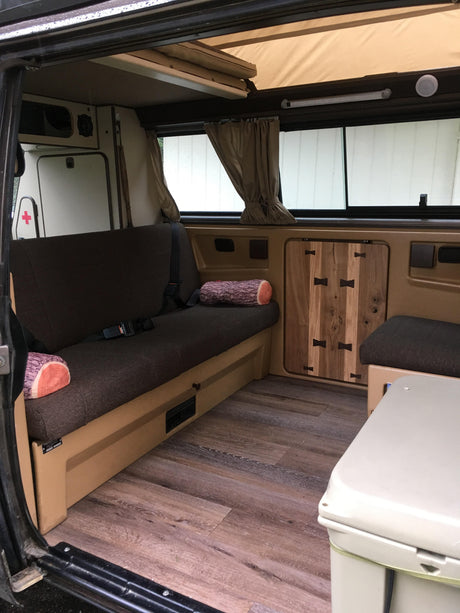 Explore this well-equipped RV rental camper van interior featuring a pop-top bed, comfortable seating, wood floor, and custom storage.