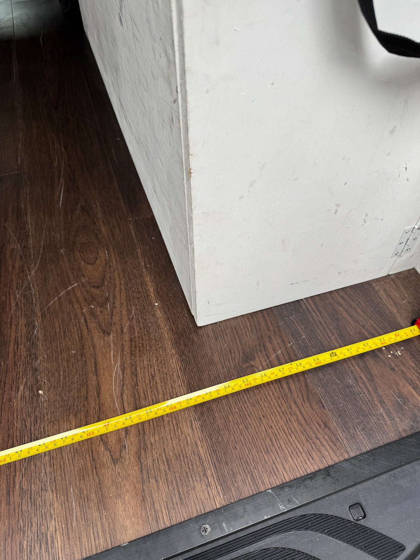 RV rental: Measuring interior floor space. Yellow tape on wood floor shows 55+ inches next to a white storage box.