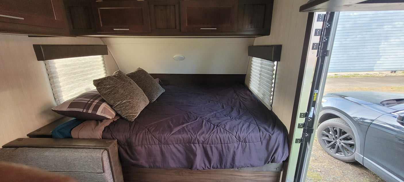Experience an RV rental! This modern RV bedroom features a comfy bed, cabinets, and an open door showing the car outside.