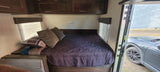 Experience an RV rental! This modern RV bedroom features a comfy bed, cabinets, and an open door showing the car outside.