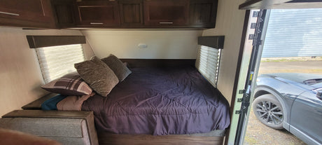 Experience an RV rental! This modern RV bedroom features a comfy bed, cabinets, and an open door showing the car outside.