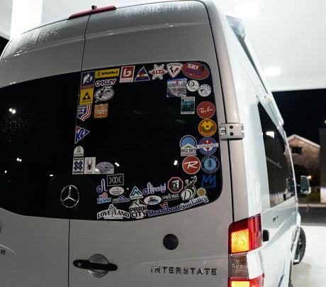 An Airstream Interstate rv rental's rear window, covered in ski resort and outdoor brand stickers from various adventures.