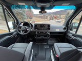Inside a modern rv rental van: driver's view of dashboard, steering wheel, seats, and a scenic road ahead.