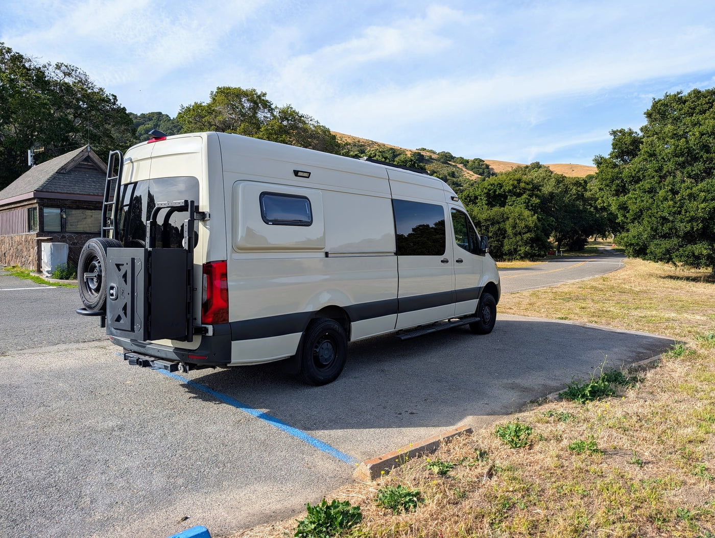 Spacious, customized camper van, likely an RV rental, parked with a rear ladder and spare tire mount, in a natural setting. — photo 7