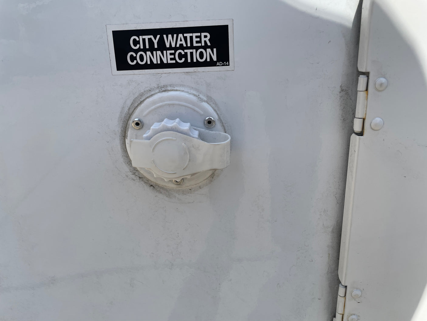 White RV rental exterior with a black "CITY WATER CONNECTION" label and water inlet, plus a door hinge on the right.