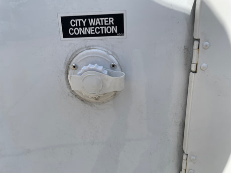 White RV rental exterior with a black "CITY WATER CONNECTION" label and water inlet, plus a door hinge on the right.