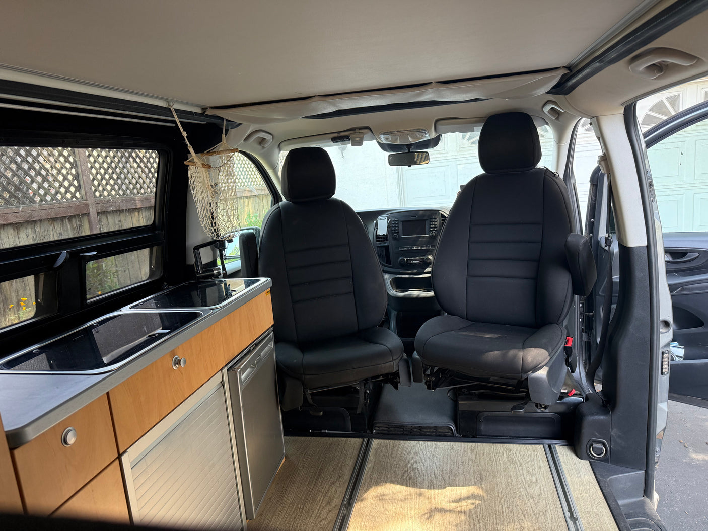 Interior of an RV rental featuring front seats, a kitchen area with sink and cooktop, integrated fridge, and wood flooring.
