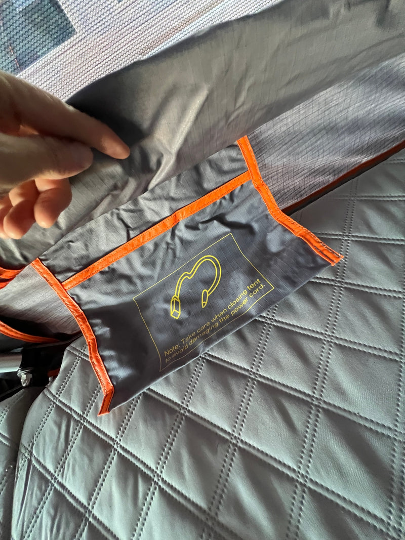 RV rental interior: a safety note on a pouch warns to protect the power cord when closing the tent, by quilted bedding. — photo 11