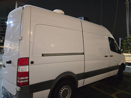 White RV rental van, converted into a camper with roof AC and vent, parked at night, rear-side view.