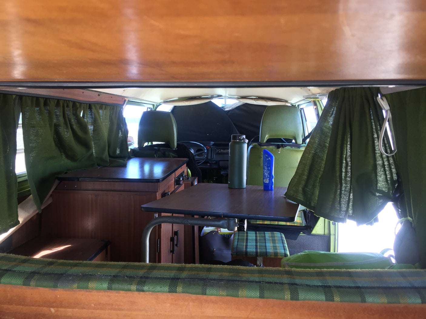 Cozy vintage camper van interior: dining area with wooden table & green curtains, ready for an rv rental adventure.